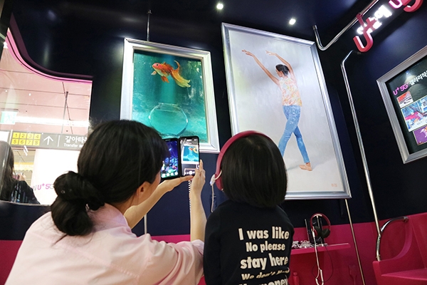 서울 지하철 6호선 공덕역에 마련된 세계 첫 5G기반 문화예술 공간 'U+5G 갤러리'에 방문한 고객이 'U+AR' 앱으로 작품을 체험하고 감상하는 모습.(사진=LG유플러스)